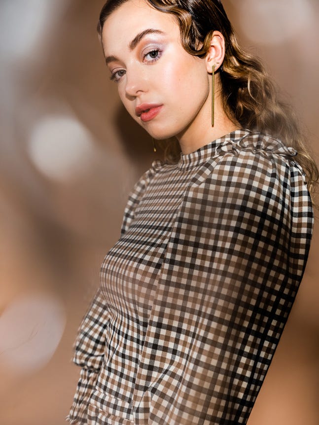 Model in brown, checkered dress, against blurred, brown background