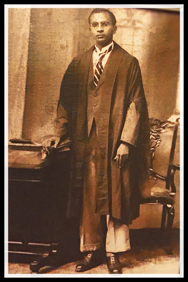 An aging brown and white photograph shows a bespectacled Asian man standing next to a desk in chair, wearing the robe of an attorney.
