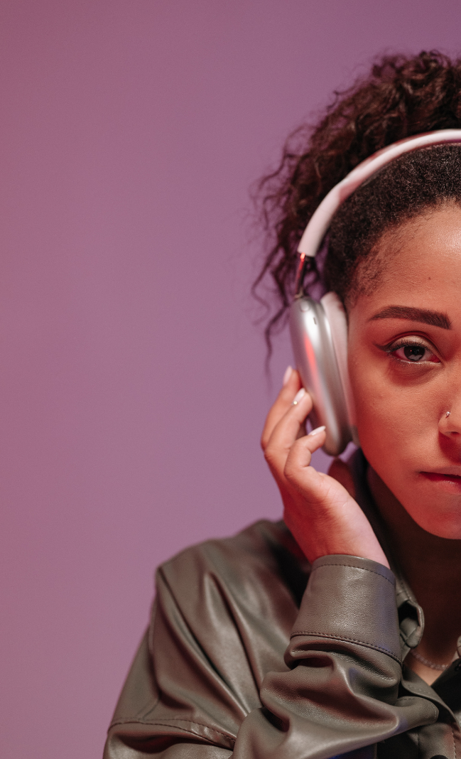 Half a portrait of a Black woman who has her hair tied back and is wearing a leather jacket and headphones.