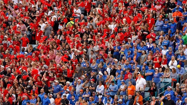 A stadium with fans wearing blue shirts in one section standing next to a section with fans all in red.