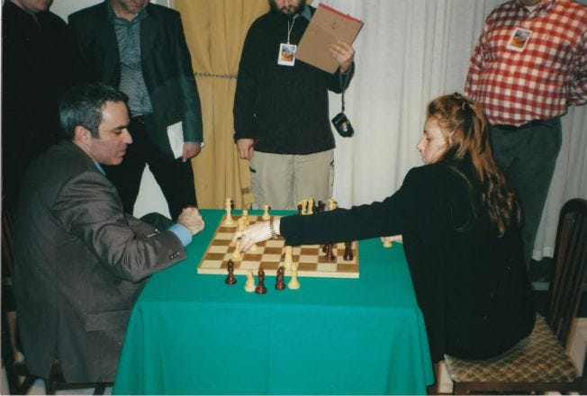 Judit Polgar is playing a chess game against Garry Kasparov with with the black pieces.