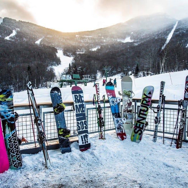 Eight snowboards lined up on a fence overlooking a ski and snowboarding run. Beautiful view of snowy mountain downhill slope towards the valley.