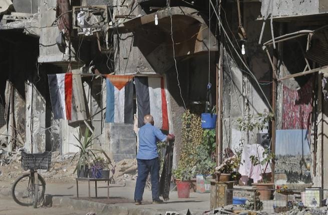 Un hombre sacude una alfombra junto a edificios destruidos del campo de refugiados palestinos de Yarmuk, al sur de Damasco, el 1 de noviembre de 2018. (Foto: Luai Beshara / AFP)