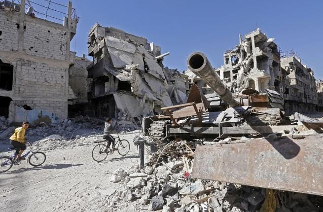 Unos niños conducen sus bicicletas entre un tanque y edificios destruidos del campo de refugiados palestinos de Yarmuk, al sur de Damasco, el 1 de noviembre de 2018. (Foto: Luai Beshara / AFP)