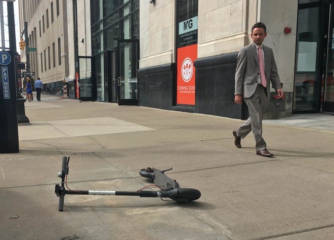 man in business suit walks by bird scotter, on its side and blocking the sidewalk