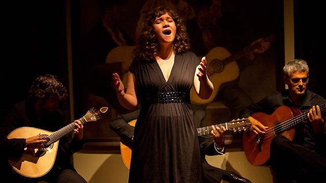 A female fado singer accompanied by a guitar player and a viola player.