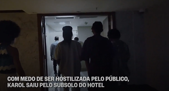 Karol e a família saindo do hotel para voltarem para casa e os dizeres na tela “com medo de ser hostilizada pelo público, Karol saiu pelo subsolo do hotel.”