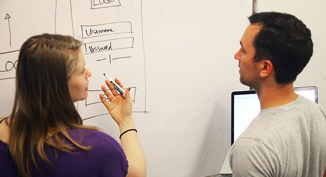 Woman holding a pen, explaining a whiteboard diagram to a man.