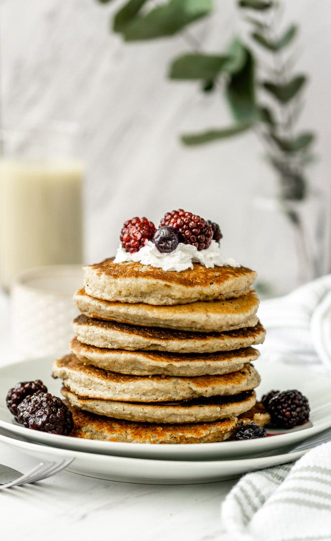 stacked pancakes made with almond flour and topped with whipped cream and berries.