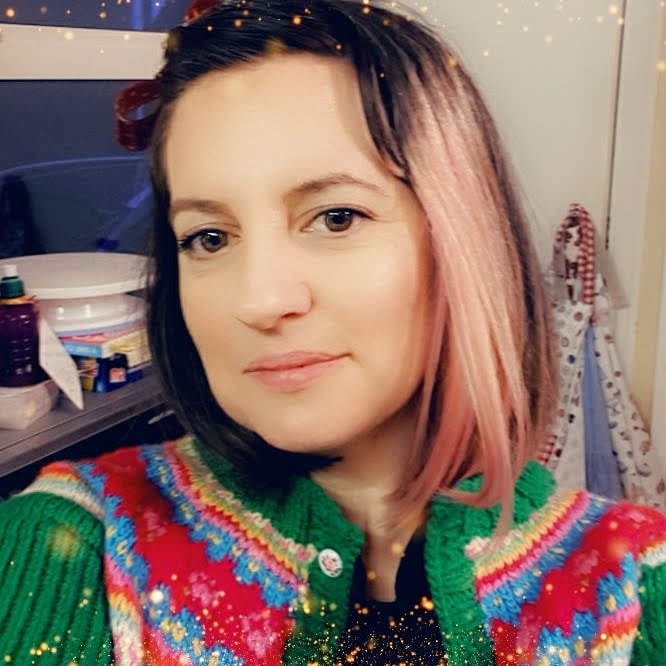 A selfie of Gemma looking at the camera, wearing a fairisle cardie in a very messy kitchen.