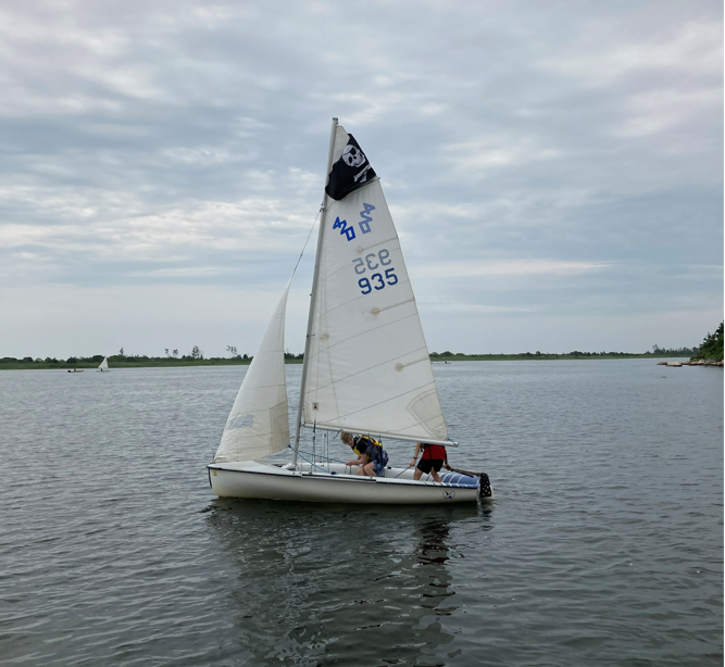 Two people in a sailboat on a pond.