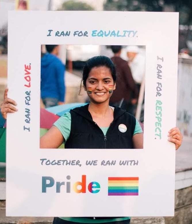 Image of a person smiling holding up a Pride sign.