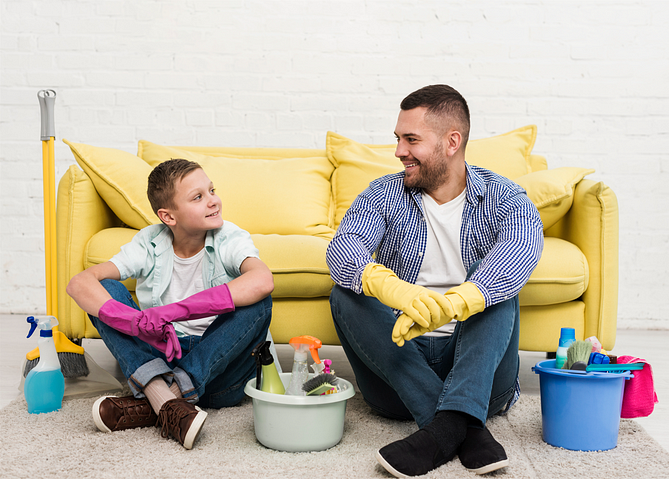 Father and son resting with cleaning products in front of them, sharing a moment of pause from chores.