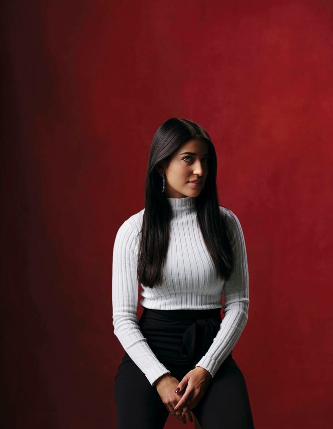 West Asian model sitting against red backdrop