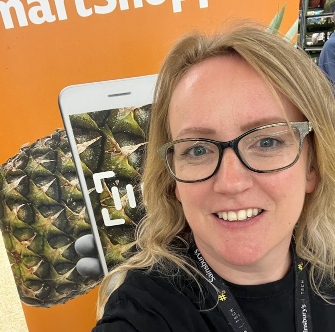 A photo of Vicky smiling in front of a photo of a pineapple being scanned by a phone.