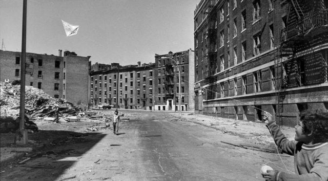 An almost empty street in the Bronx, NYC, with only a child holding a kite, circa 1970s