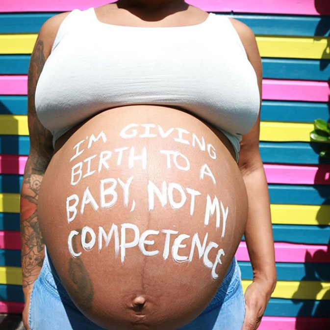 A pregnant woman with ‘I’m giving birth to a baby, not my competence’ written in white across her stomach.