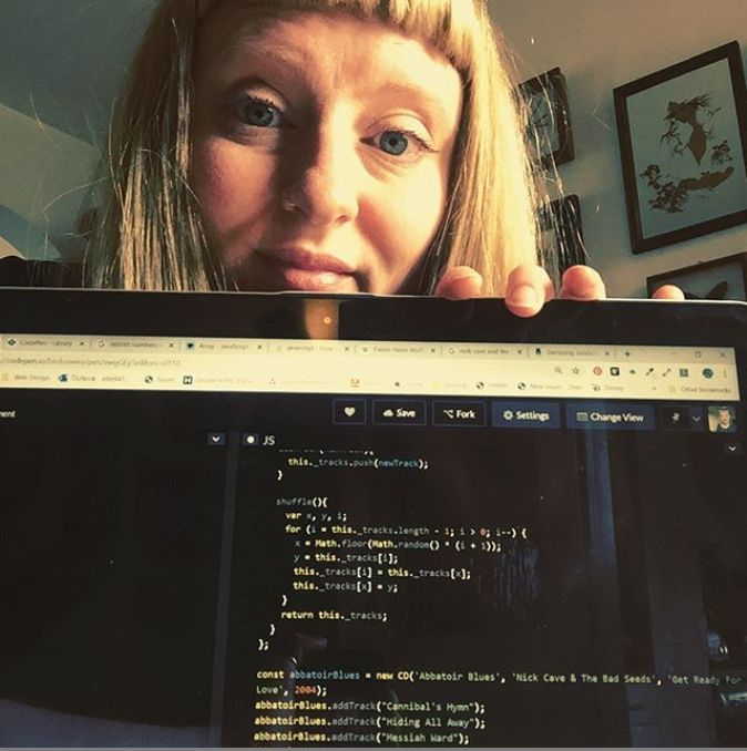 Ellie sits with her laptop in front of her, the screen is displaying JavaScript shuffle algorithm.