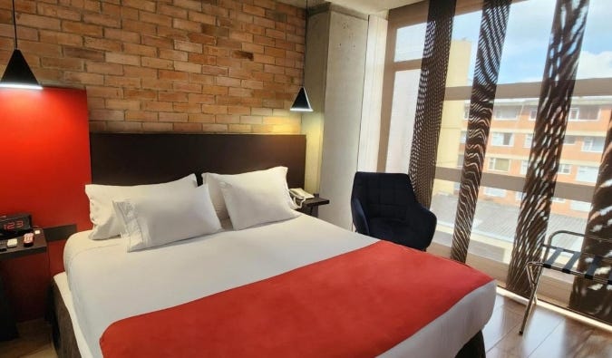 Simple guest room with a double bed in front of an exposed brick wall at Hotel 5 Elementos Apartasuites in Bogotá, Colombia
