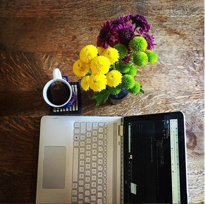A bird’s eye view of laptop, cup of tea and fresh cut flowers on a table