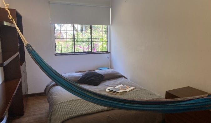 Simple room at Magdalena Guest House in Bogota, Colombia, with a double bed, wooden wardrobe, window, and hammock strung across the room