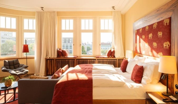 A guestroom with lots of historic windows and a large bed with a red fabric headboard embroidered with the signature elephant of Orania, a five-star hotel in berlin, germany