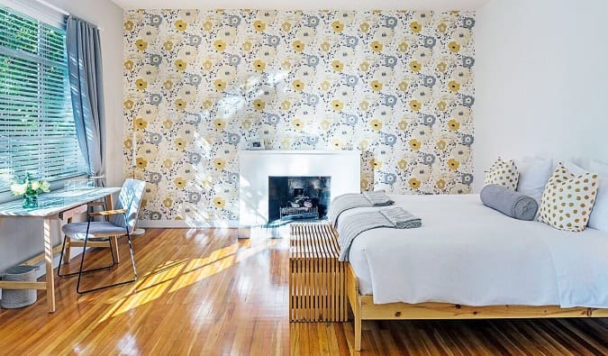 A light-filled guest room with floral wallpaper, a fireplace, hardwood floors, desk, and crisp white queen bed at Casa Legado in Bogotá, Colombia