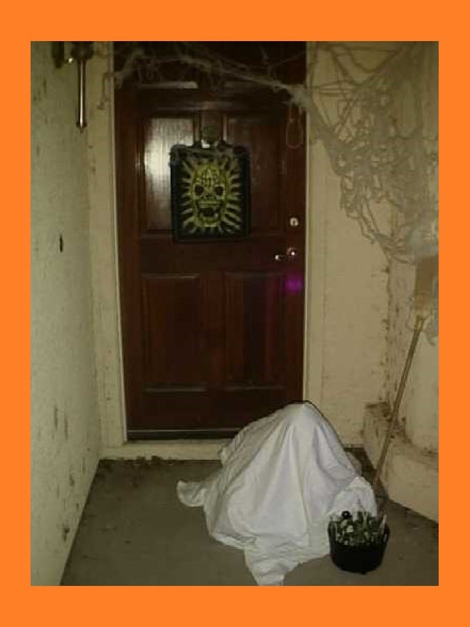 Halloween scene: “Ghost” with a goody bucket sitting in front of a decorated doorway