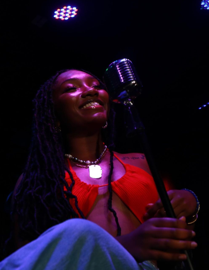 A young, female spoken word poet smiles while sitting in front of a microphone.