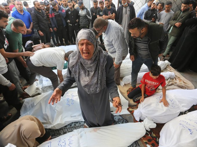 A imagem mostra um grupo de palestinos no chão assassinados e cobertos. Há uma senhora palestina, em pá, em destaque na fotografia e no meio dos corpos, o que evidencia ter perdido algum conhecido.