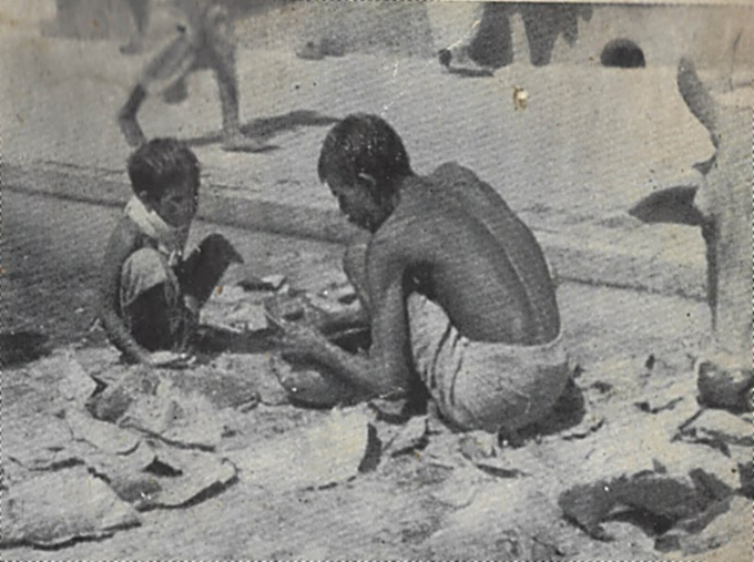 Uma fotografia em preto e branco de uma família empobrecida e faminta em Bengala, por volta de 1943. A rua está suja e precária, assim como as pessoas presentes na foto, visivelmente desnutridas.