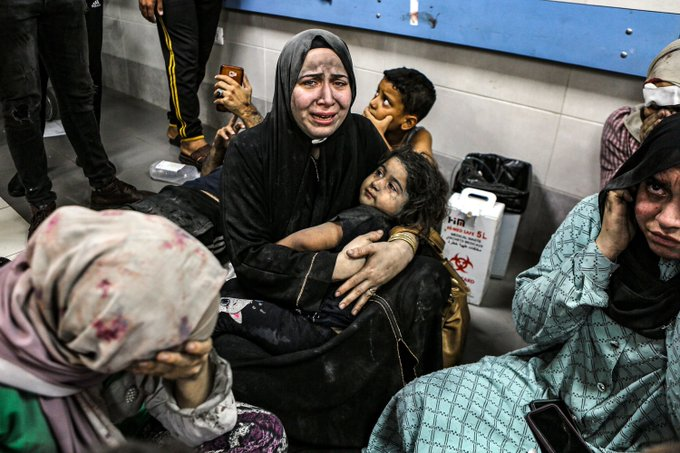 A imagem mostra um grupo de palestinos e palestinas sentados no chão de um ambiente fechado, que parece ser um hospital em Gaza. O conteúdo inclui resíduos hospitalares. Essas pessoas estão chorando pelo sofrimento e pelas perdas que tiveram. Todos estão sentados.