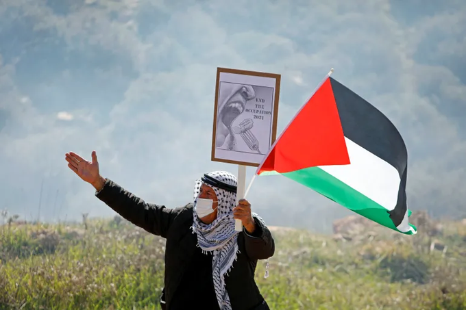 Um manifestante palestino mascarado segura uma faixa e uma bandeira palestina durante um protesto contra os assentamentos israelenses, em Beit Dajan, na Cisjordânia ocupada por Israel