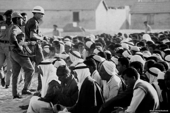 A fotografia, em preto e branco, mostra soldados israelenses na frente de um grupo de vários palestinos da Cisjordânia sendo intimidados e sentados por esses militares. O cenário parece ser ao ar livre, com a pessoa e a multidão no chão.