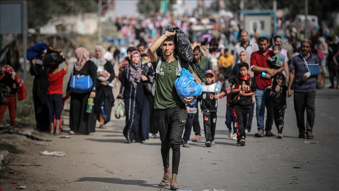 A fotografia mostra uma multidão de palestinos deslocando-se num evento que se dá o nome de Nakba de 2023, visto o número de refugiados, deslocados e desalojados palestinos na Faixa de Gaza desde o novo genocídio do povo palestino iniciou em outubro. O cenário é ao ar livre, mostra palestinos caminhando pelo asfalto das ruas. Palestinos de diferentes idades e recortes sociais que são deslocados.