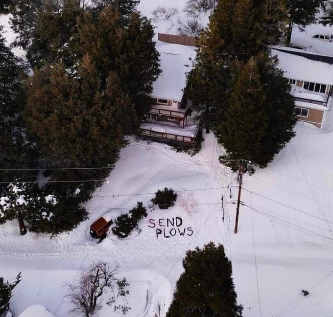 Aerial view of a message written in the snow in Crestline California that reads: “Send Plows”