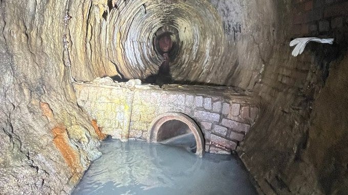 a brick sewer from 1873. a regulator wall with water visible flowing towards a pipe and away from the camera.