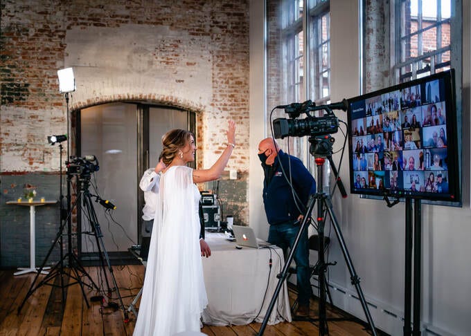 Bride waves to Zoom wedding guests on a large screen at a 2020 Covid Wedding.