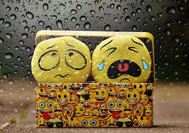 Worry face and crying face emojis peeking out of a box on a rainy day