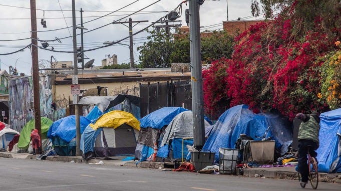 A row of blue homeless tents line a city street.