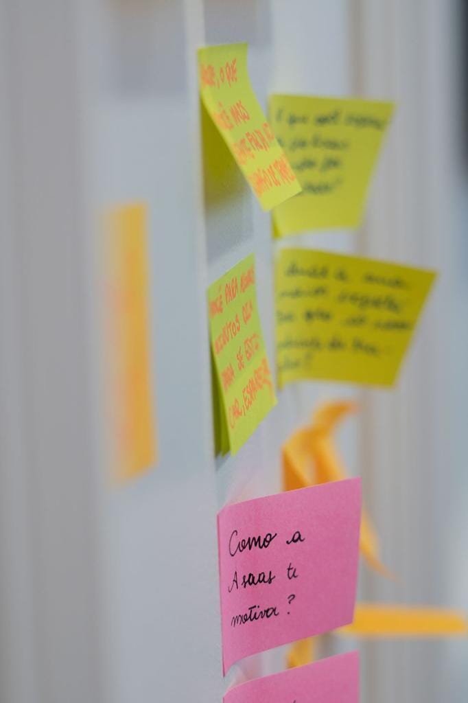 Foto de uma parede branca com post-its coloridos. É possível ler, em um dos post-its, a mensagem “Como a Asaas te motiva?”.