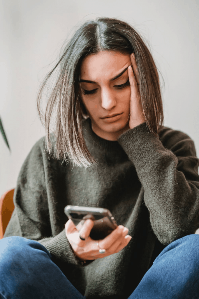 A woman in an olive sweater looking at her phone to know who is calling