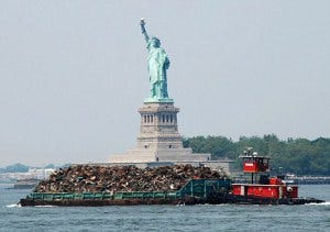 A tug boat pushes a garbage barge past the Statue of Liberty