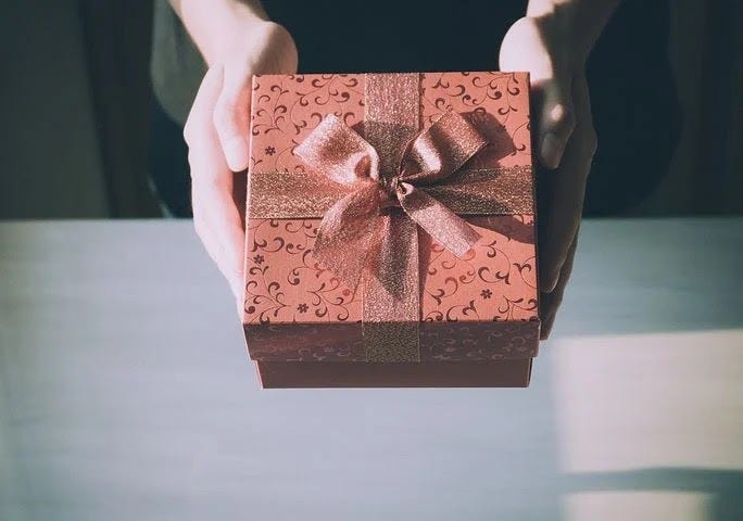Picture show hands of a person holding a gift wrapped in red paper.