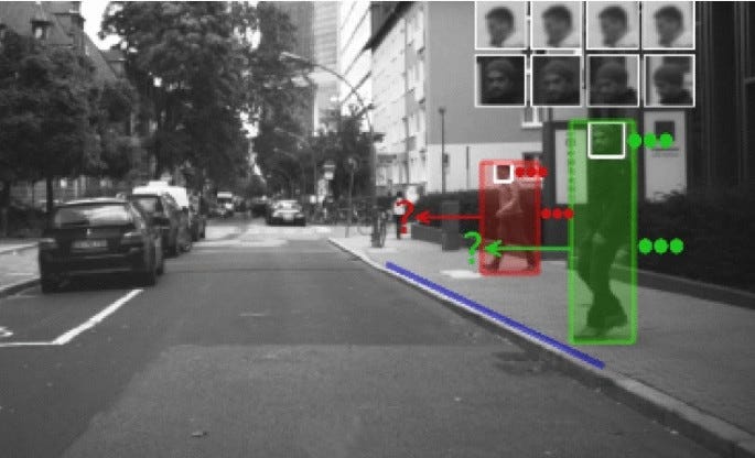 The image appears to show a street scene with computer vision technology identifying pedestrians. Boxes, color-coded in red and green, highlight two people, possibly tracking their movement or detecting potential hazards