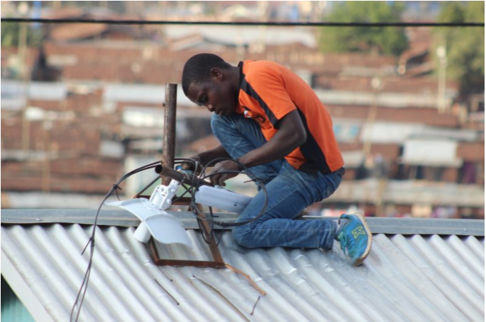 In the urban slums of Kenya, a man installs a networking equipment on the roof of a building.