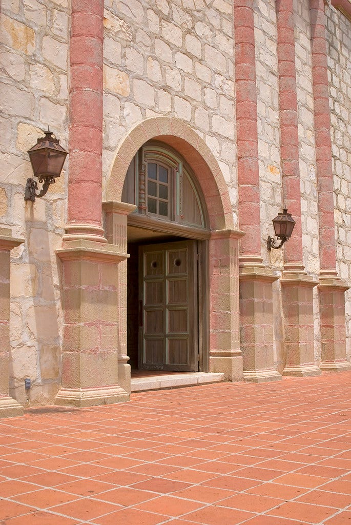 An open door in a pink limestone building.