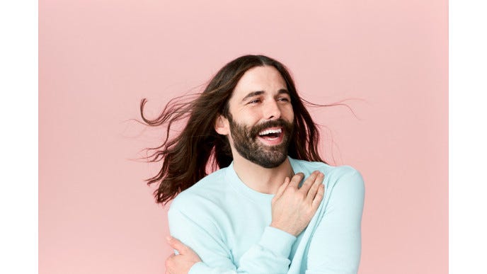 Photo of Jonathan Van Ness smiling against a bright pink background.