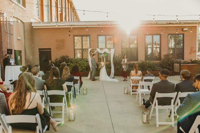 Bride and groom stand before their guests at an outdoors, masked and socially distant 2020 Covid Wedding.