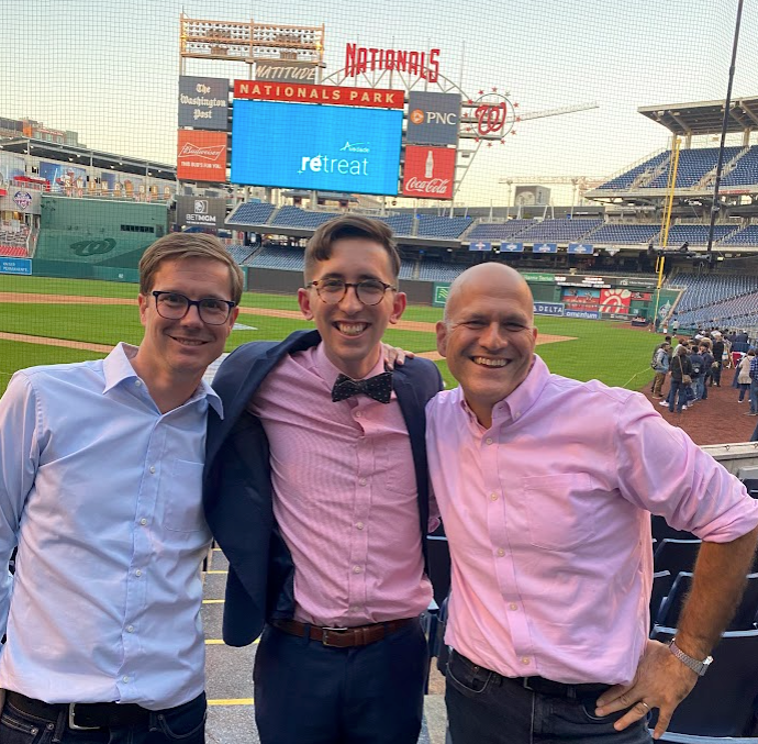 Aledade President Mat Kendall, Doug, and Aledade CEO Farzad Mostashari standing in front of homeplate at Nationals Park in Washington, DC with the Aledade logo on the jumbotron in the background.